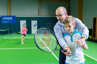Poika harjoittelee tennistä opettajan kanssa