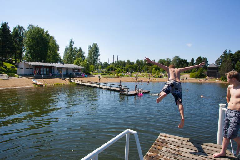 Mies hyppää uimahypyn veteen Apianniemen uimarannan laiturilta