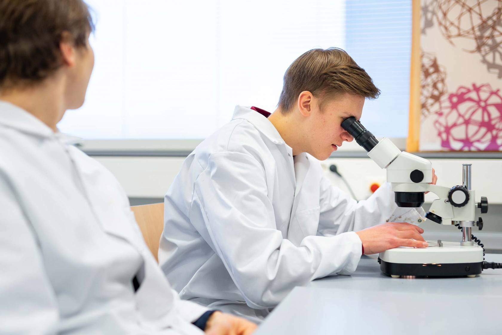 Poika katsoo mikroskoopilla näytettä oppitunnilla Tietotien lukiossa.