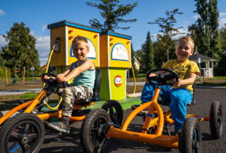 Boys are driving pedal cars.