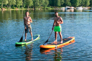 Men are stand up paddling by the lake.