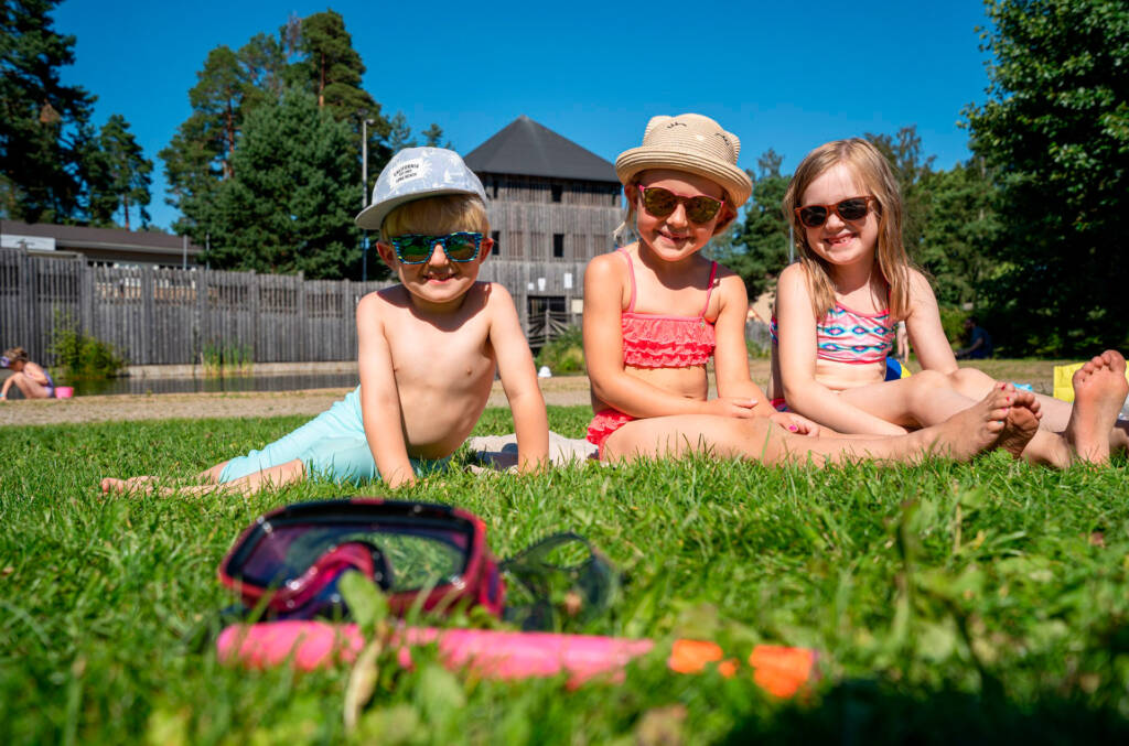 Lapset istuvat Apian uimarannalla nurmikolla ja taustalla näkyy Seikkailupuiston torni.
