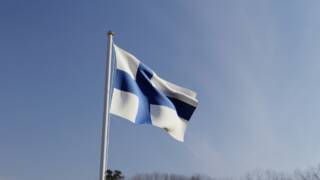Sinivalkoinen Suomen lippu liehuu tuulessa.
