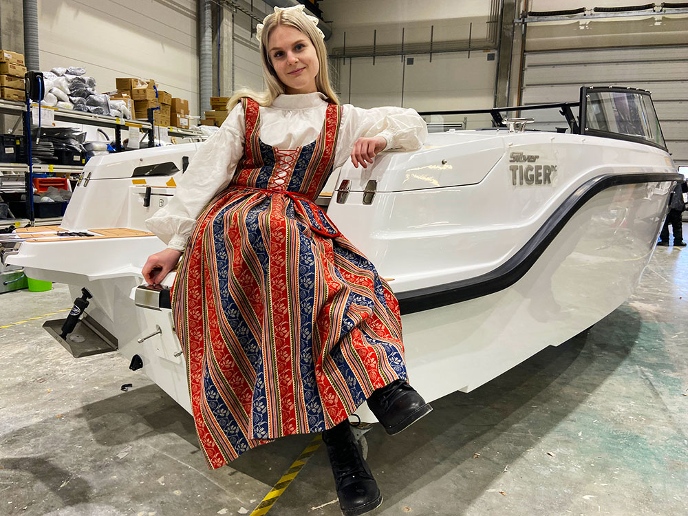 Nainen istuu veneessä Sääksmäen kansallispuku päällä venetehtaalla.