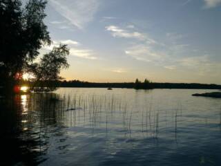 Kesäinen auringonlasku järven rannalla.