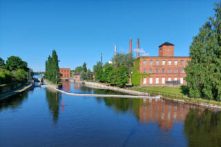 Valkeakosken kanava, etualalla vettä jossa punainen reimari. Sivussa oikealla Myllysaaren museo sekä tehtaan piippuja.