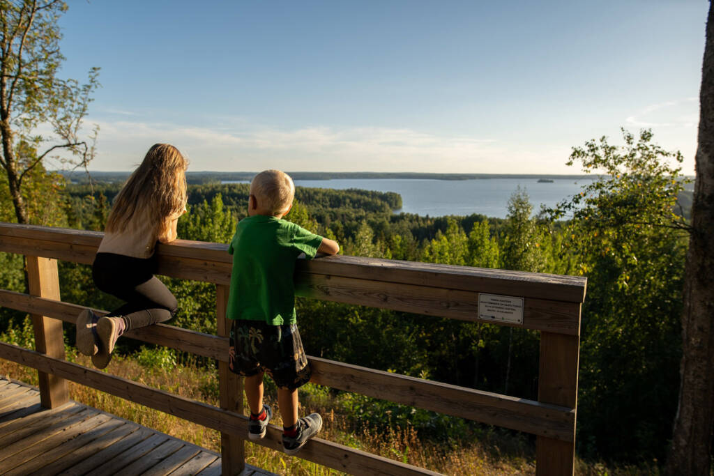 Lapset nojaavat kaiteeseen Rapolanharjun tasanteelta ilta-auringossa.