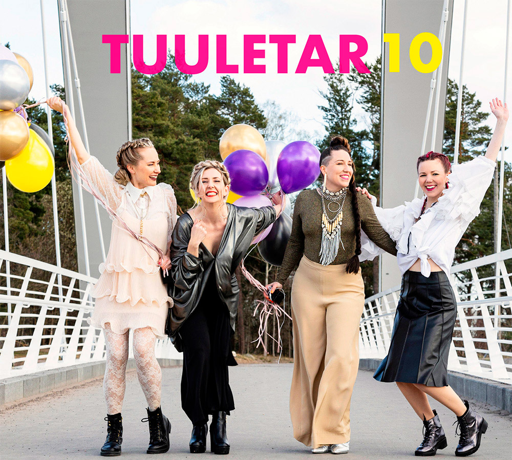 Neljä naista kävelee riippusillalla ja pitävät ilmapalloja käsissään.
