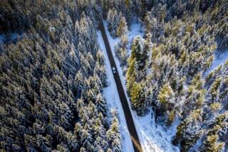 Talvinen havupuumetsä, jota halkoo maantie. Maantiellä kulkee yksi henkilöauto.