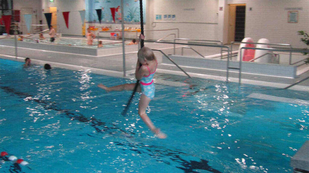 Tyttö roikkuu liaanissa uimahallin allasveden päällä.