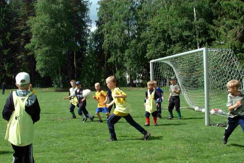 Pojat pelaavat palloa nurmikentällä.