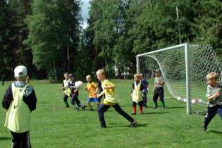 Pojat pelaavat palloa nurmikentällä.