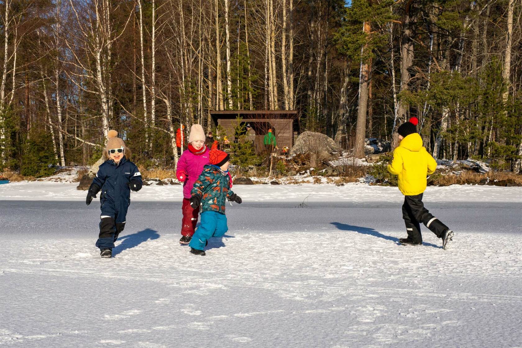 Neljä lasta juoksee järven jäällä, taustalla Pappilanniemen laavu Valkeakoskella.