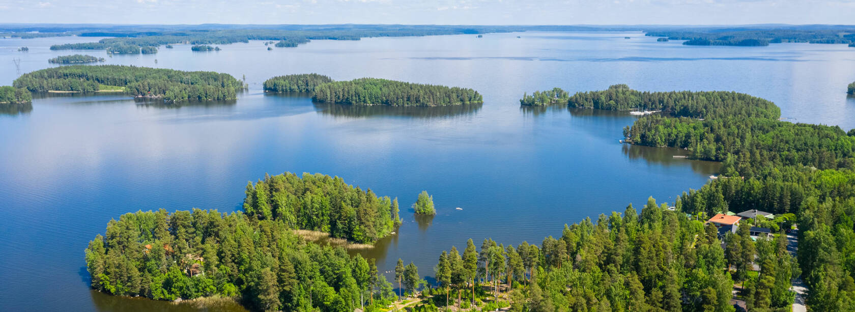 Ilmakuva, jossa näkyy järvi, metsää ja oikeassa alareunassa taloja.