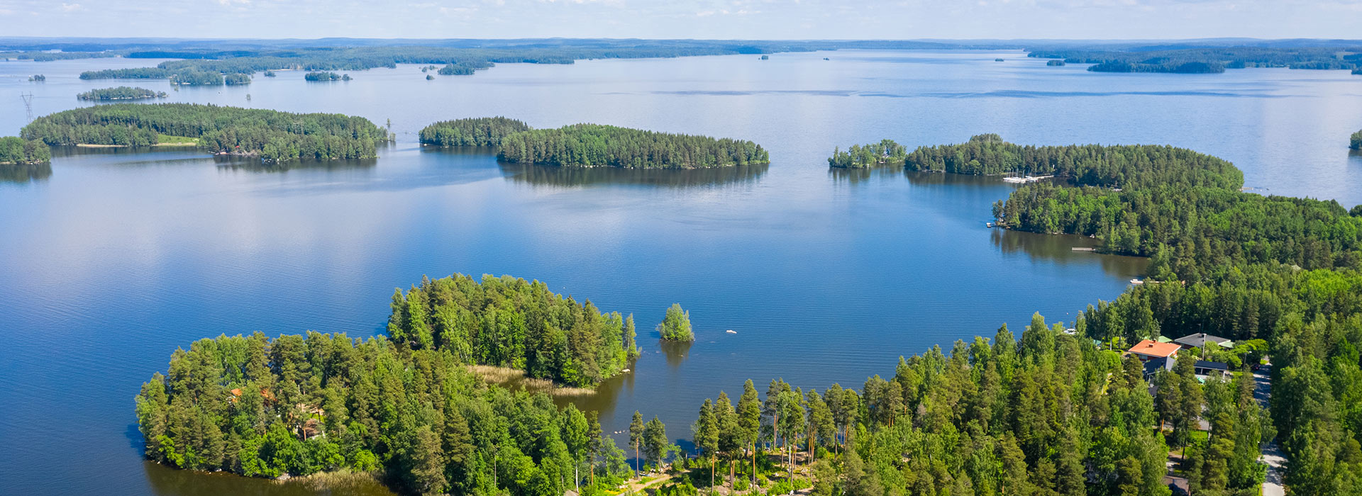 Ilmakuva, jossa näkyy järvi, metsää ja oikeassa alareunassa taloja.