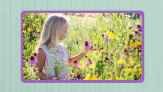 Tyttö seisoo kukkakedolla ja katselee kukkaa.