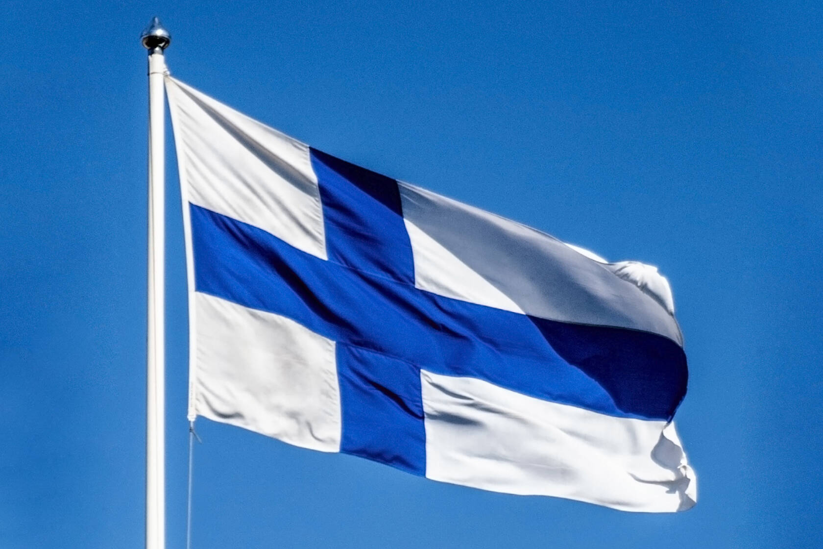 Suomen lippu sinistä taivasta vasten.
