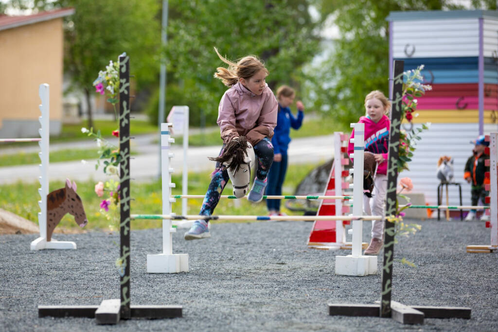 Lapsi hyppää esteen yli keppihevosen selässä.