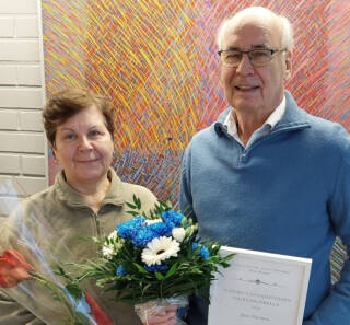 Kuvassa kaksi henkilöä, jotka pitelevät käsissään kukkia ja Vuoden vapaaehtoinen -palkintoa.