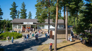 Ravintola Paviljonki Apian rakennus ja ihmisiä sen piha-alueella kauniina kesäpäivänä.