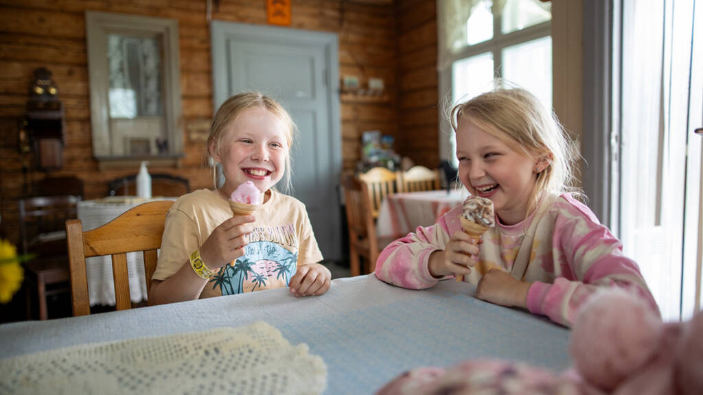 Tytöt syövät jäätelöä kahvilan pöydän ääressä.