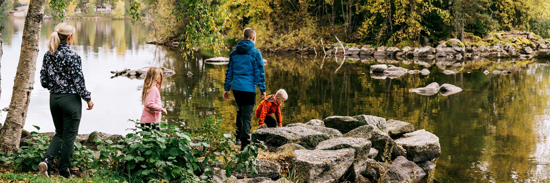 Perhe ulkoilemassa syksyisessä luonnossa järven rannalla.