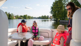 Kaksi aikuista ja kaksi lasta veneessä järvellä kaupungin keskustassa.