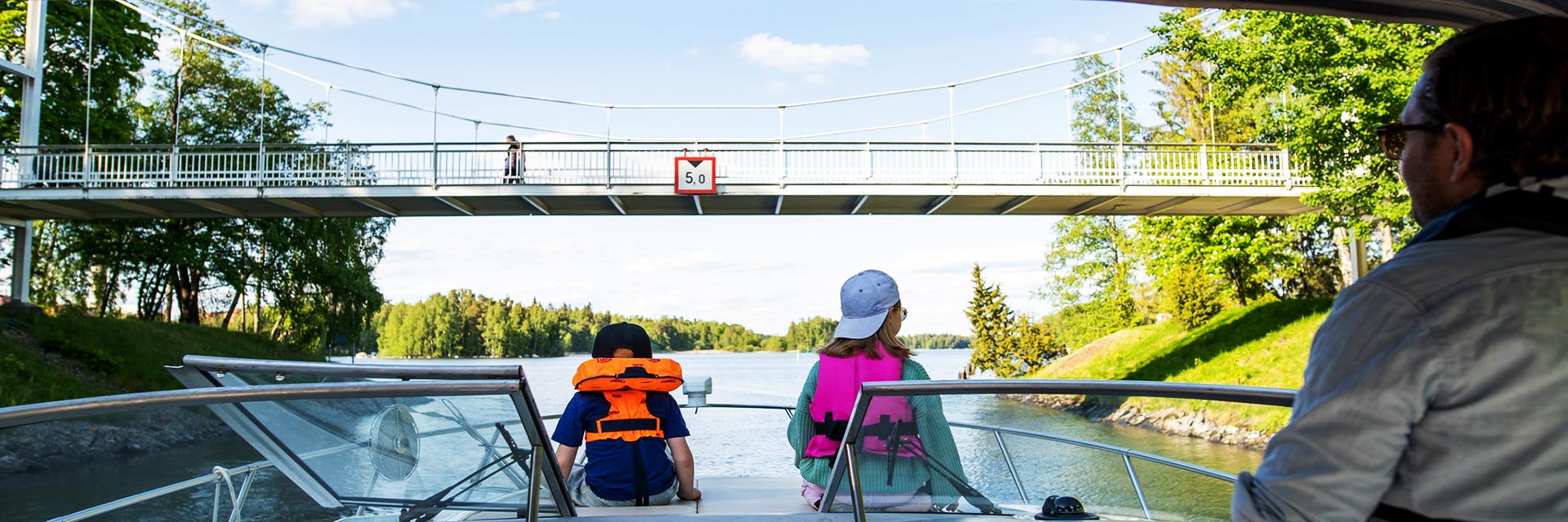 Perhe moottorivenessä lähestyy riippusiltaa.