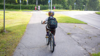 Lapsi pyöräilee pyörätiellä koulureppu selässään.