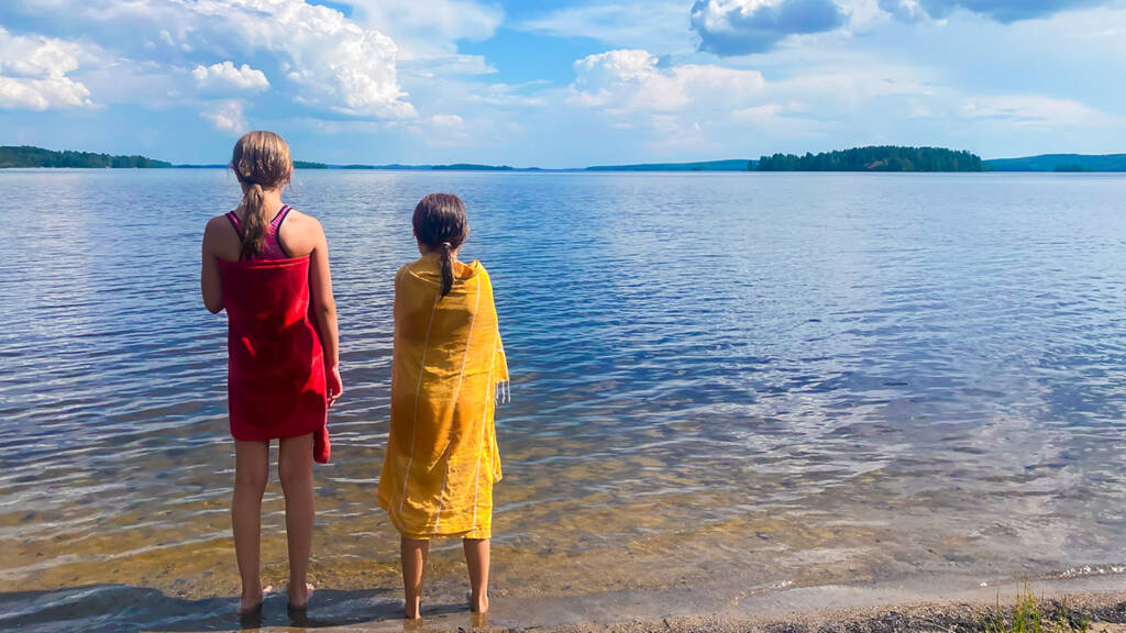 Lapset seisovat rannalla ja katsovat järvimaisemaa.
