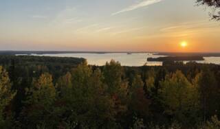Maisema Rapolan Linnavuorelta, missä näkyy järvi ja ilta-aurinko loistaa taivaalla.