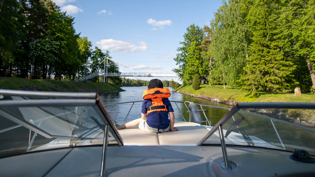 Poika katselee veneen keulassa vesille.
