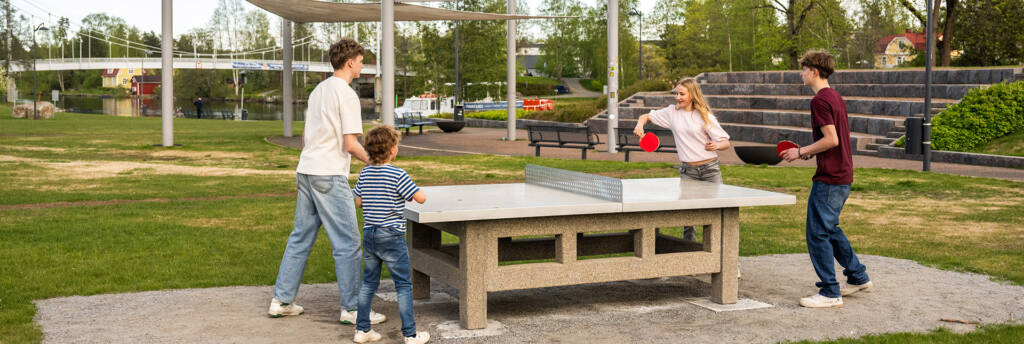 Kolme nuorta ja lapsi pelaamassa pingistä puistossa.