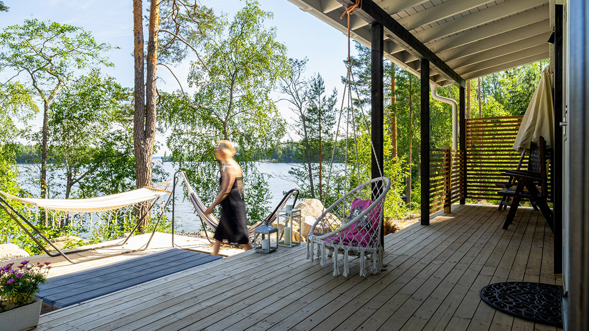 Henkilö kävelee ulkona talon terassilla ja taustalla kesäinen järvimaisema.