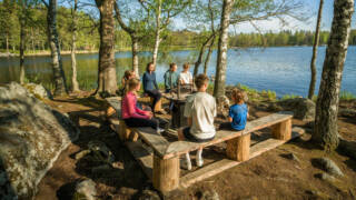 Perhe istuu järvenrannalla nuotiopaikalla.