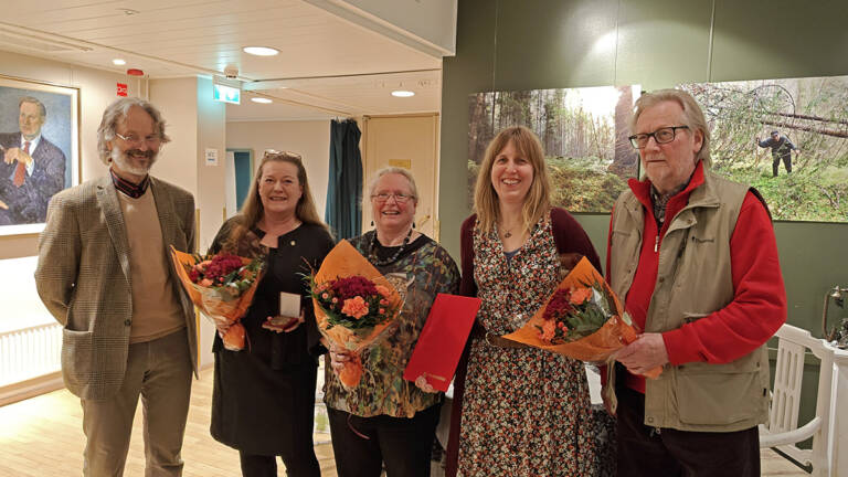 Kaksi miestä ja kaksi naista seisovat rivissä kukkakimppujen kanssa.