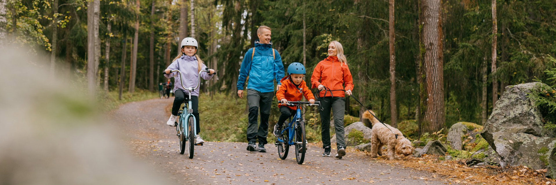 Kaksi aikuista kävelemässä koiran kanssa ja kaksi lasta pyöräilemässä ulkoilureitillä.