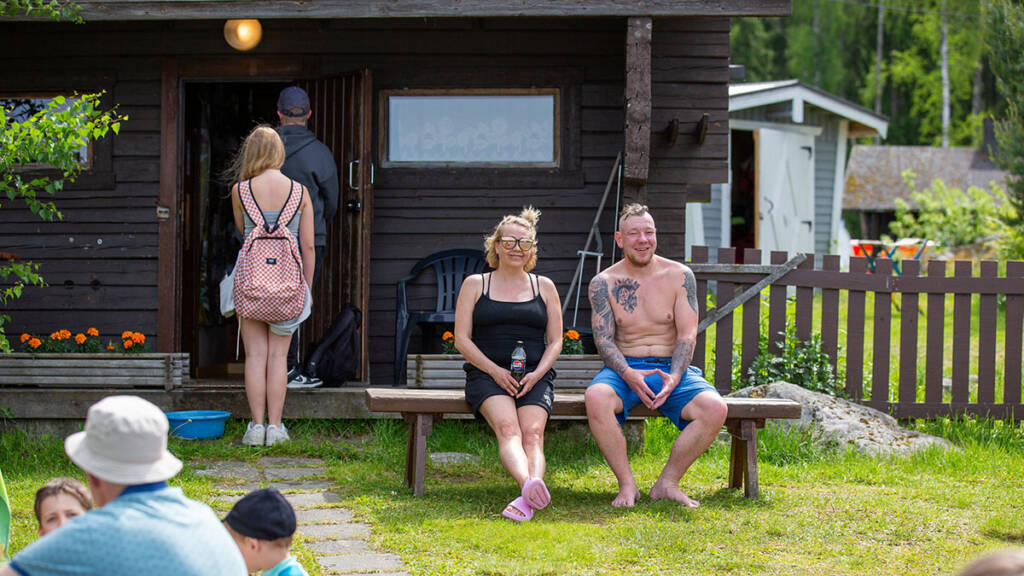 Kaksi ihmistä istuu rantasaunan edessä.