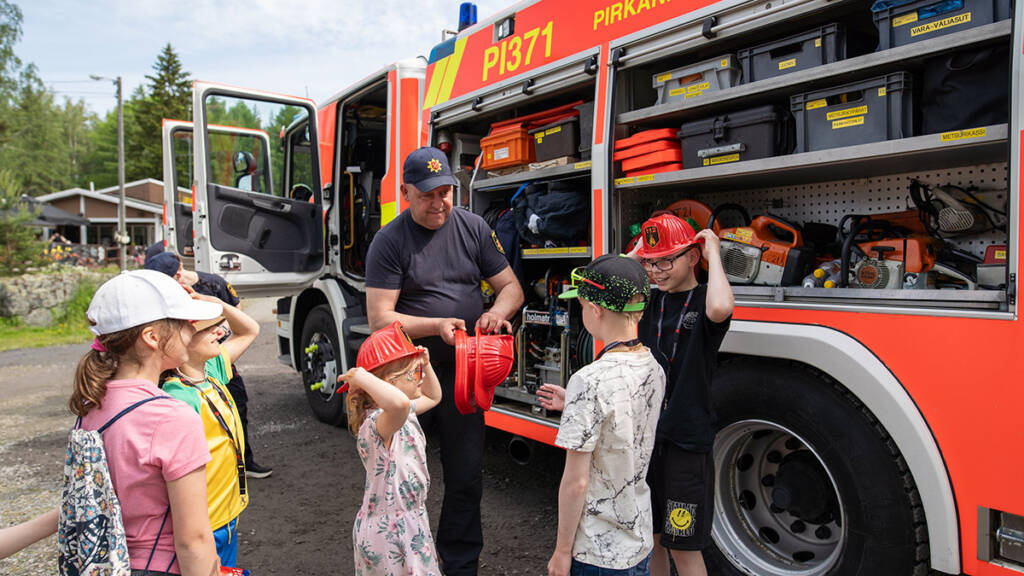 Palomies ja lapsia paloauton edessä.