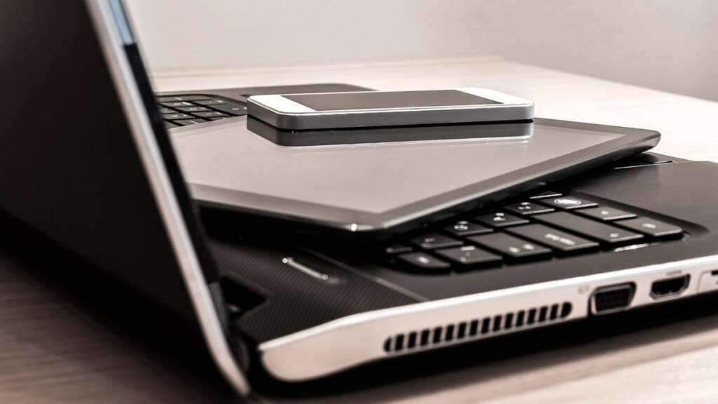 Kannettava tietokone, tabletti ja matkapuhelin pinottuina päällekäin.