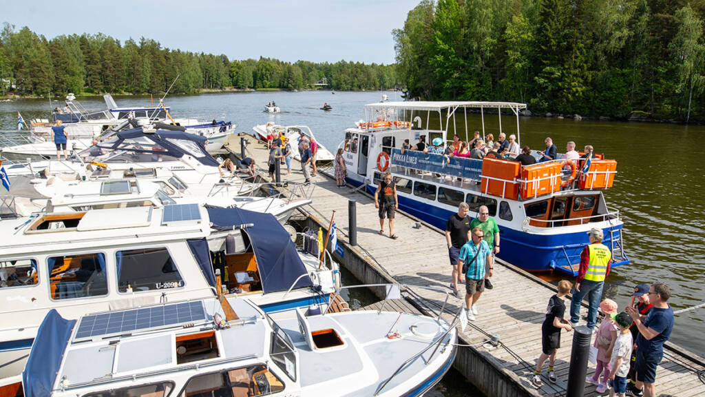 Ihmisiä, veneitä ja sisävesiristeilylaiva sataman laiturilla.