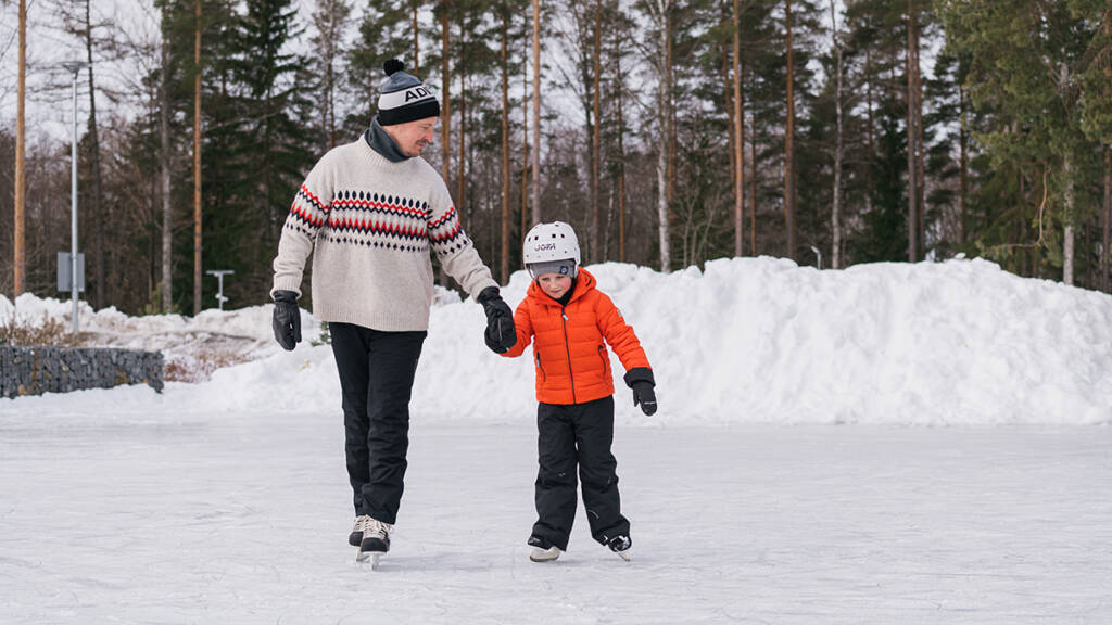 Mies ja poika luistelevat käsikädessä ulkojäällä.