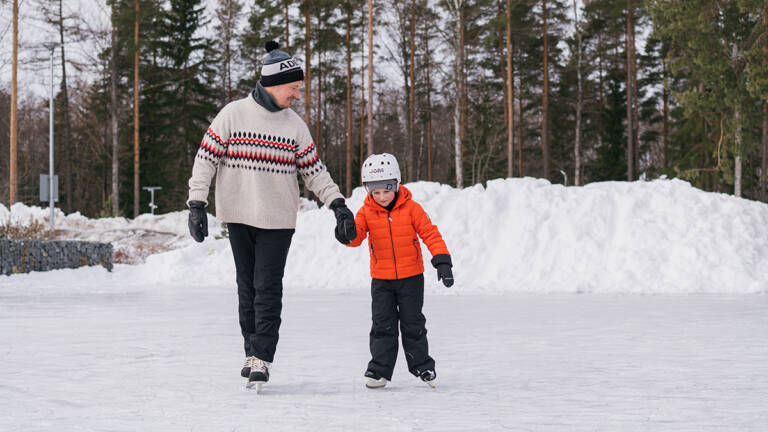 Mies ja poika luistelevat käsikädessä ulkojäällä.