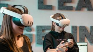 kaksi nuorta naista vr-lasit päässä pelaamassa.