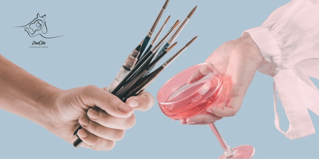 Vasemmalla käsi pitää siveltimiä ja oikealla kädessä on viinilasi.