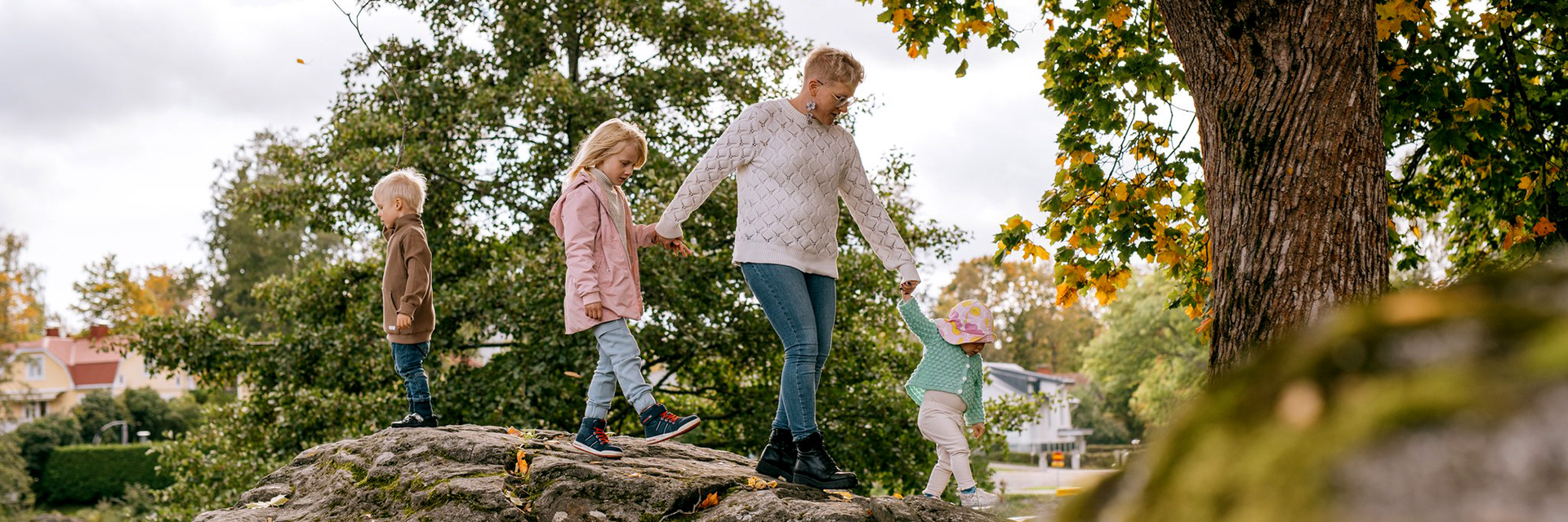 Äiti ja kolme lasta kiipeilevät käsikädessä kivien päällä puistossa.