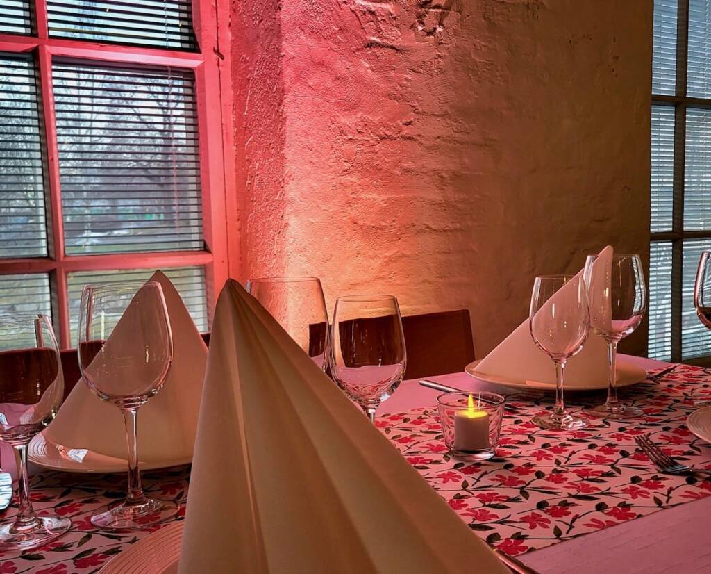 Pinkissä valaistuksessa pöydälle on katettuna viinilaseja ja lautasliinoja.