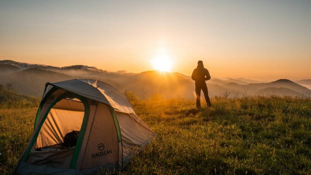 etualalla teltta ja taaempana retkeilijä auringonnousua katselemassa