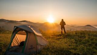 etualalla teltta ja taaempana retkeilijä auringonnousua katselemassa