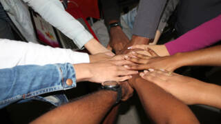 Ryhmä ihmisiä asettaa kätensä päällekkäin keskelle yhteistyön merkiksi.